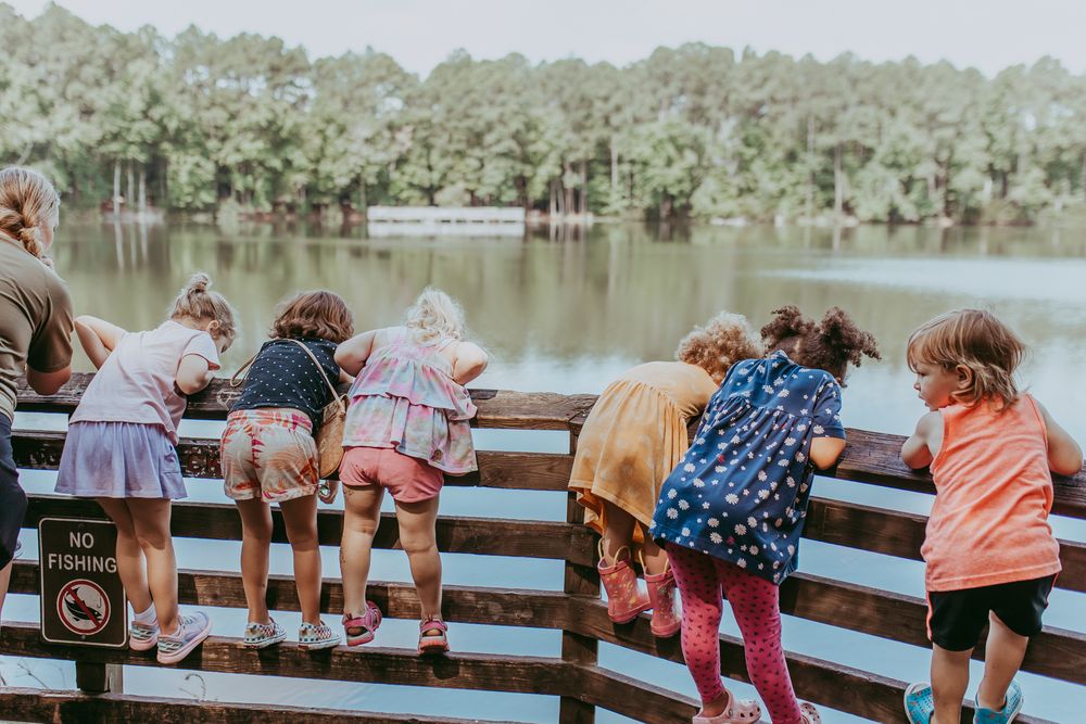 Children lean over a wooden railing at a lake while enjoying a summer day outdoors. Whitney Popp, Arizona photographer