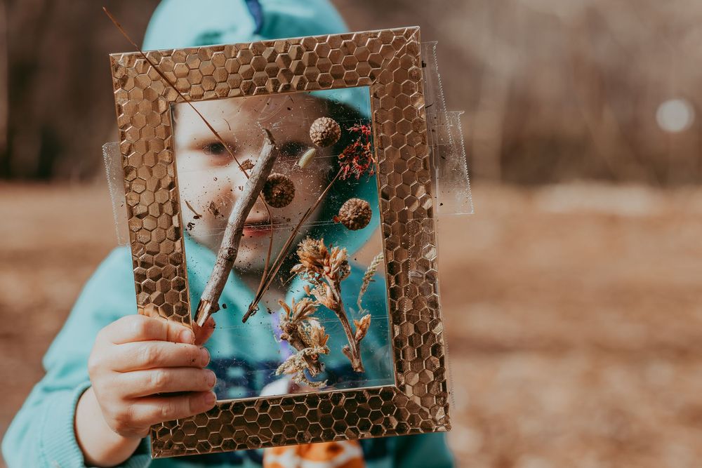 Someone in a teal sweater holds up an ornate picture frame with dried flowers and leaves in an outdoor autumn setting. Whitney Popp, Arizona