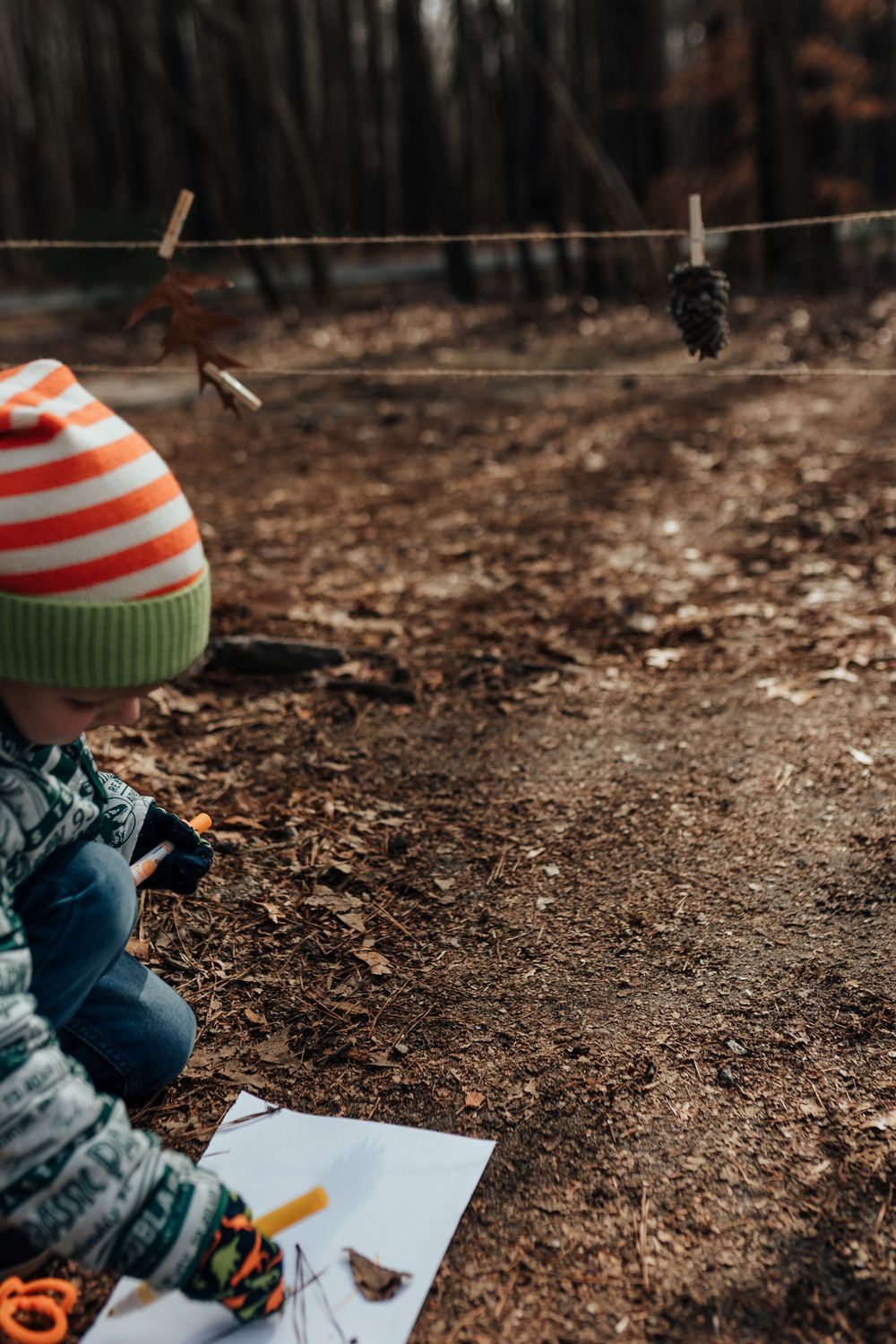 A child wearing a striped winter hat draws on paper while sitting on the ground in an outdoor autumn setting. Whitney Popp, Arizona