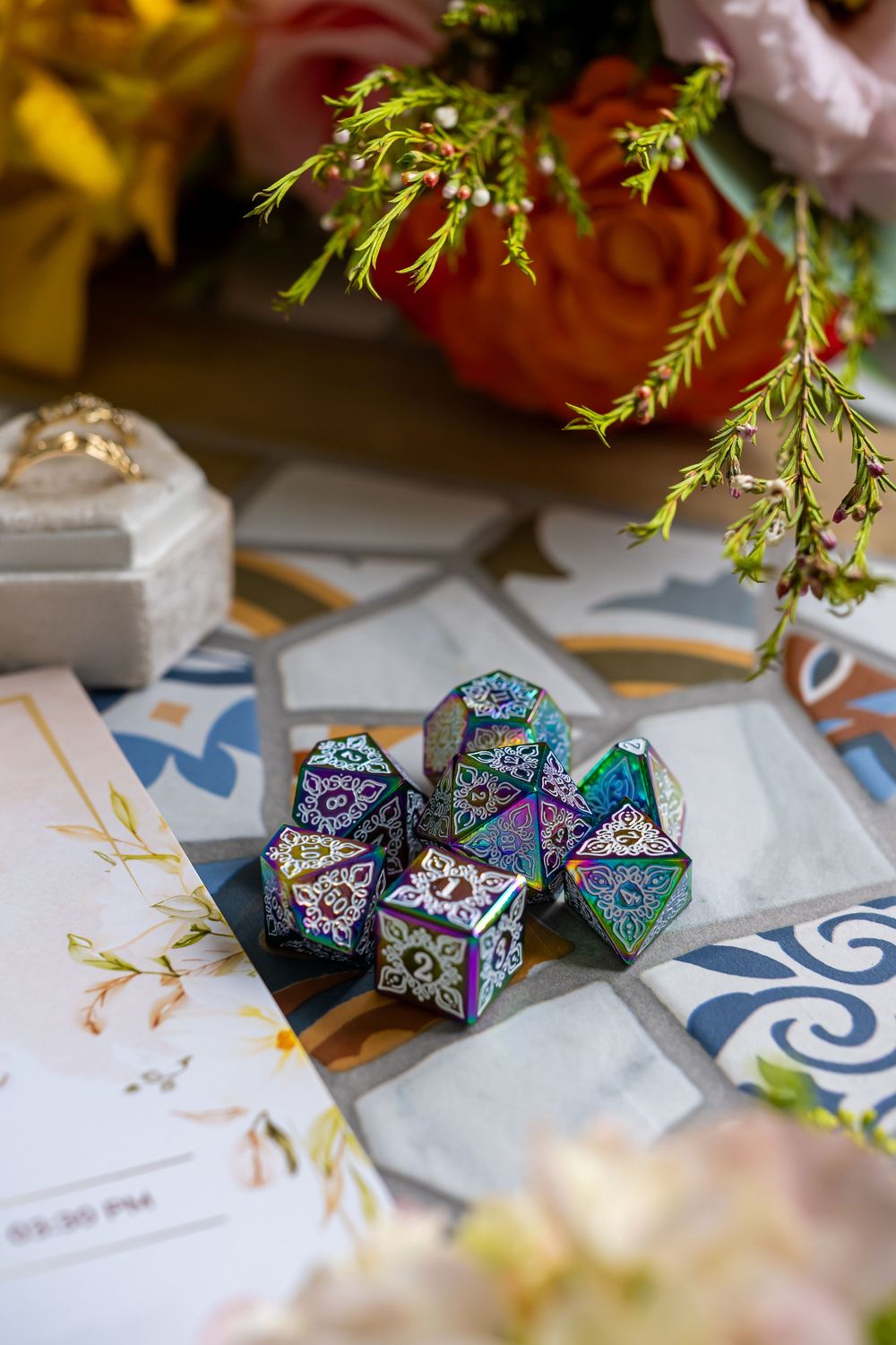 Colorful iridescent gaming dice with floral designs displayed on patterned tiles with delicate greenery.