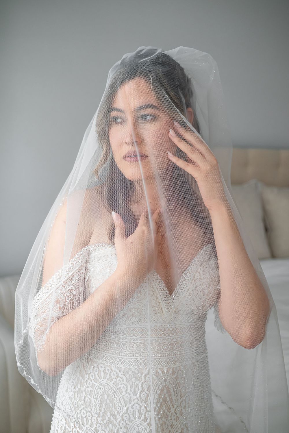 Ethereal bridal portrait with delicate lace dress and sheer veil in soft window light.