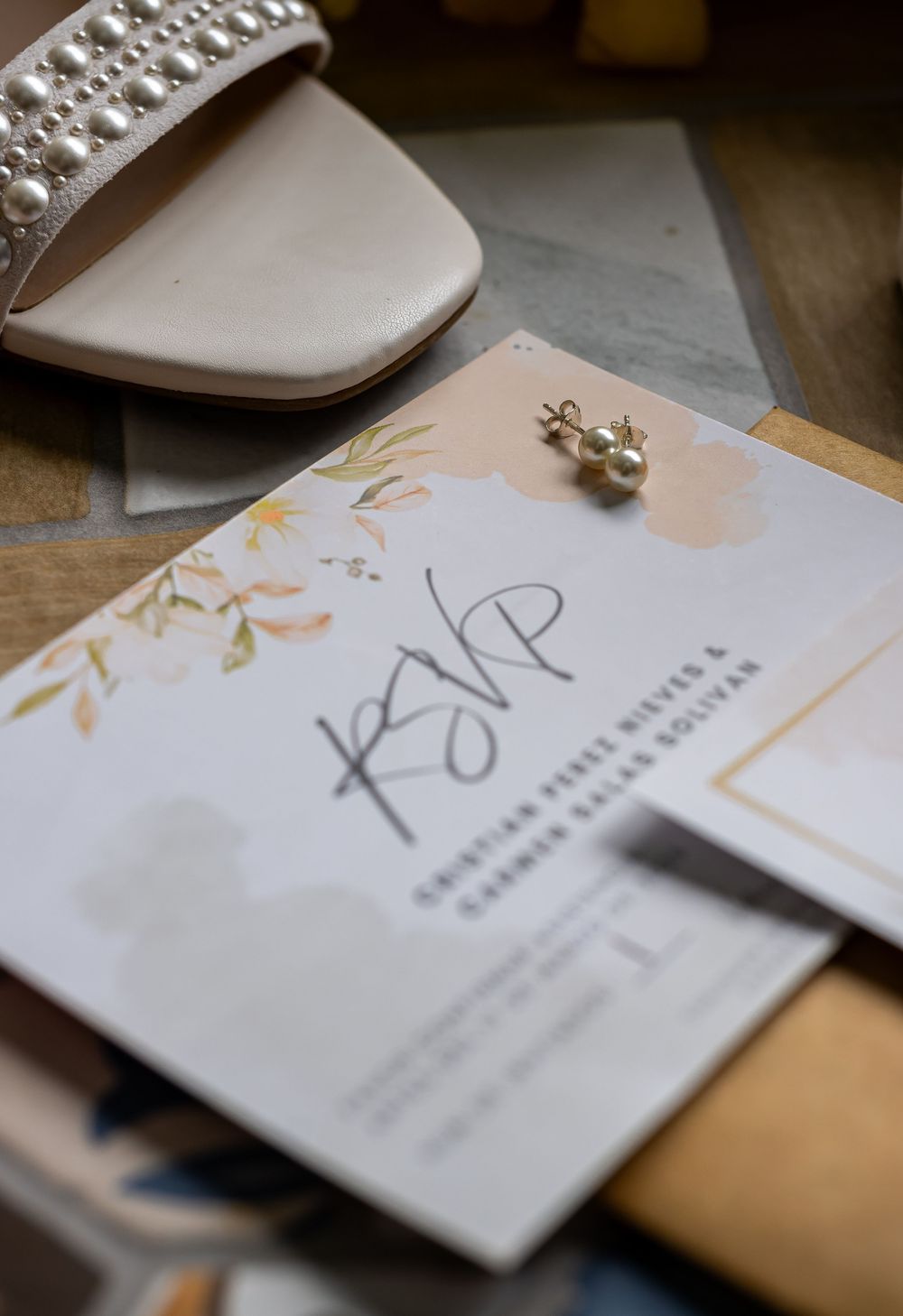 Wedding invitations with elegant calligraphy and pearl embellishments displayed on a wooden surface.
