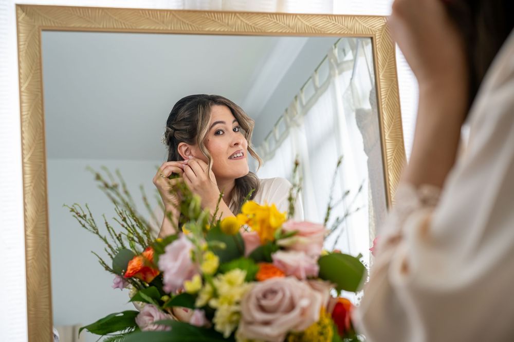 Person smiling while arranging flowers with pink and yellow blooms in an indoor setting.