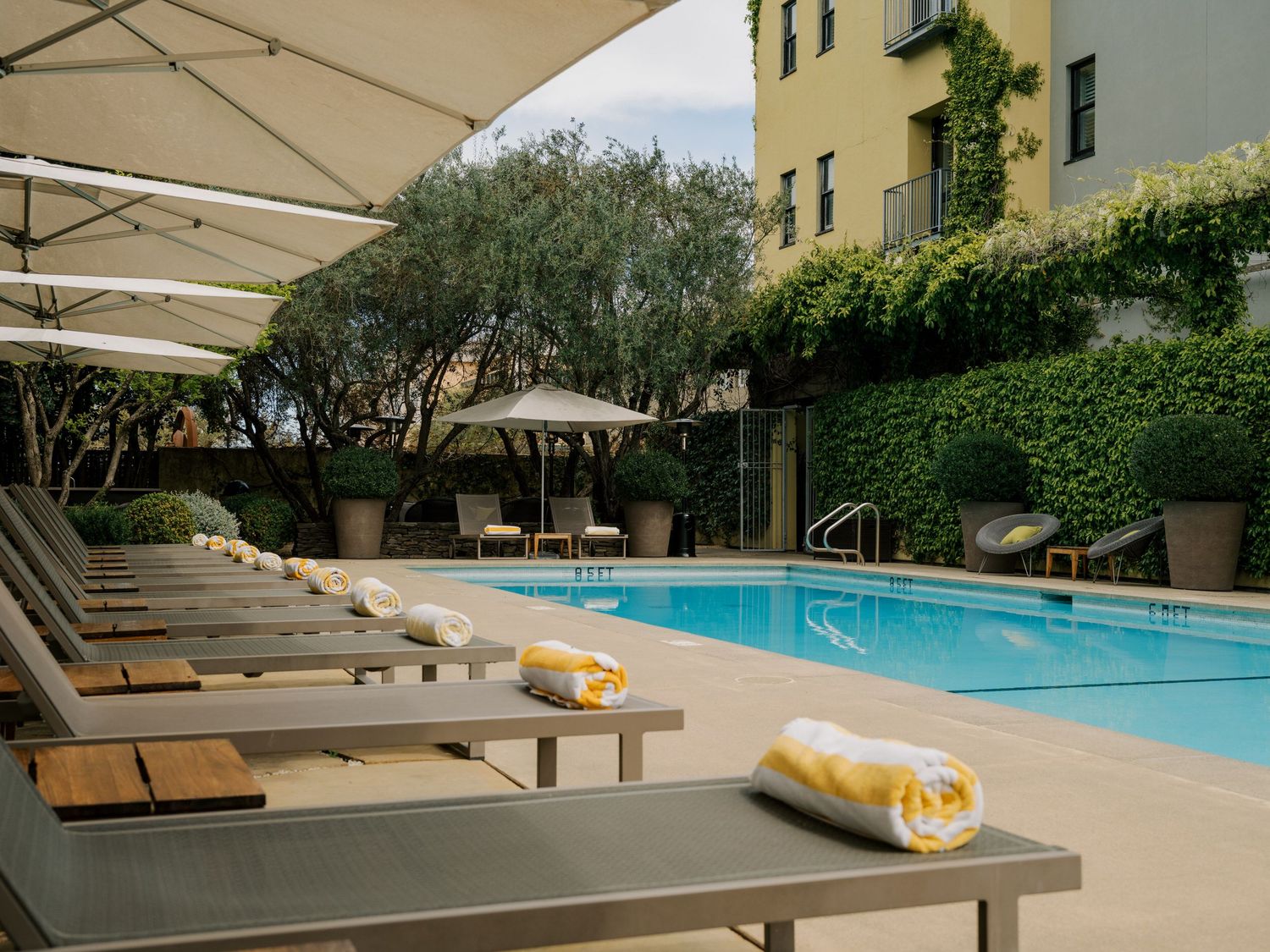 Luxury poolside lounge chairs with beige umbrellas line a tranquil swimming pool at an upscale resort.