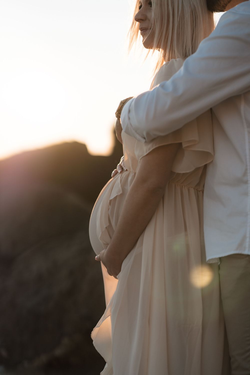 Side view of an intimate maternity photo with a person in a flowy beige dress during golden hour sunset.