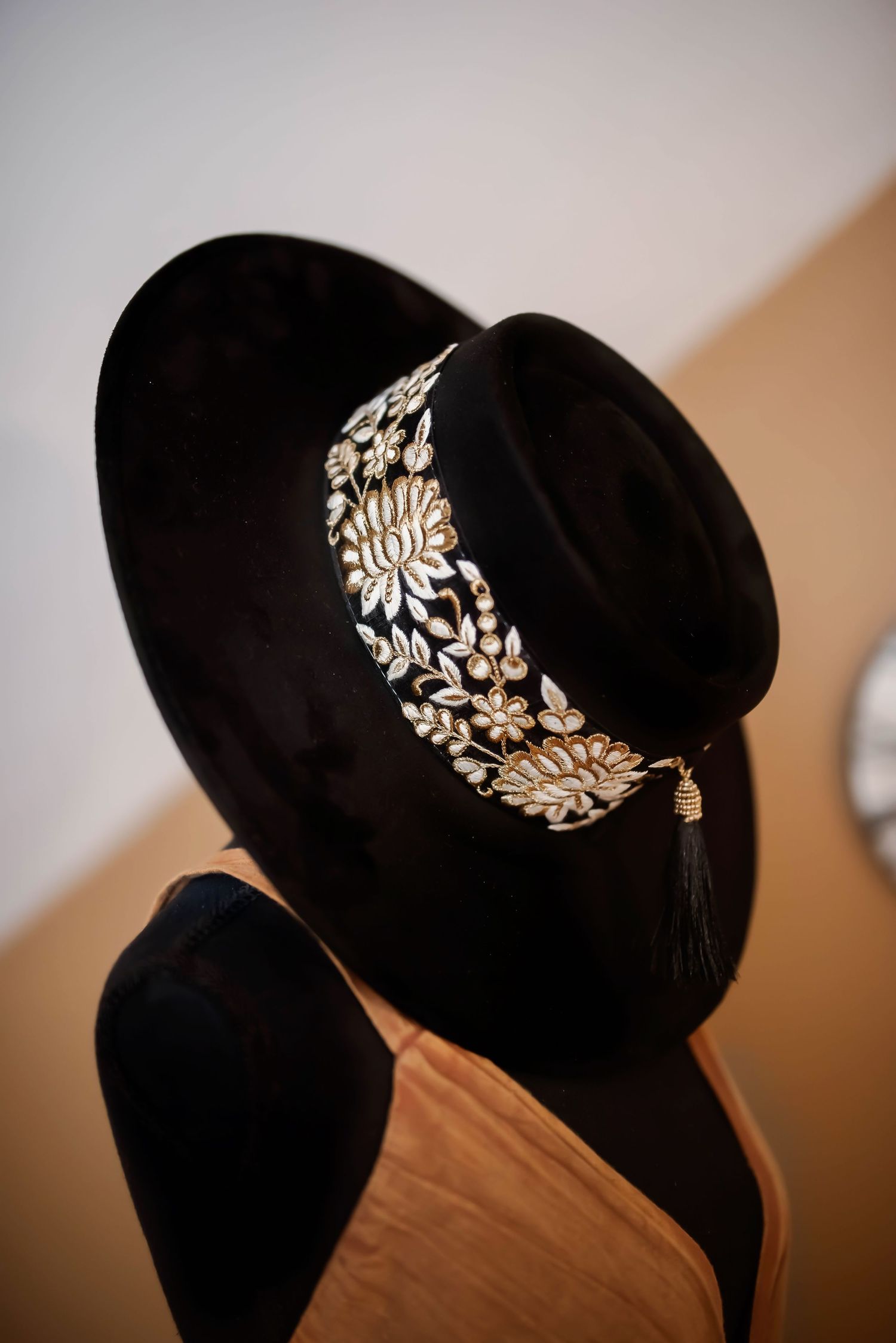 Black velvet hat with ornate silver floral embellishment band displayed against warm lighting.