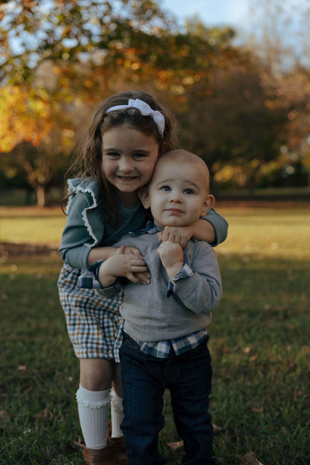 Two children playing together on grass during a golden autumn afternoon in a park setting.
