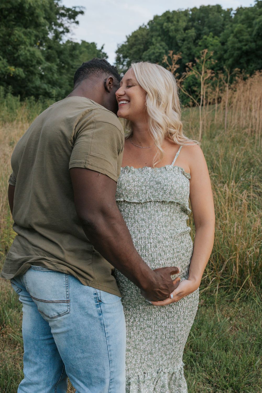 Couple embracing and laughing together in a grassy field during golden hour.