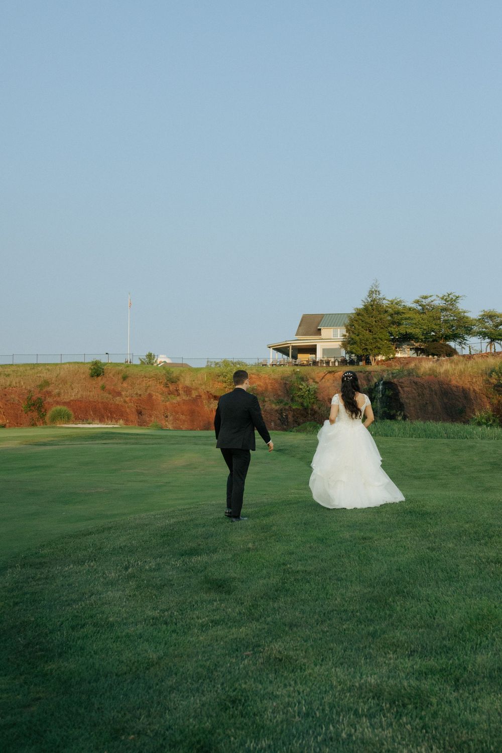 A newlywed couple walking together on a scenic hilltop overlooking the water at sunset.