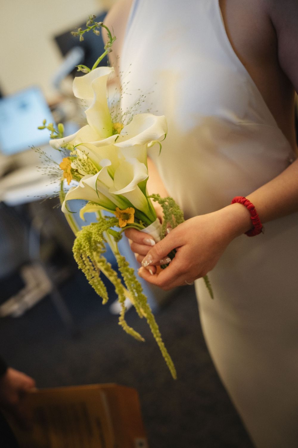 A person in a white dress holds an elegant bouquet of white calla lilies with delicate green foliage.