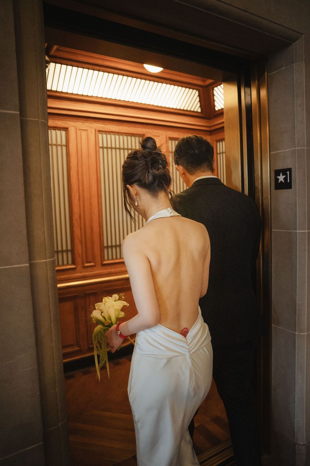 A couple in white bathrobes walking down a warmly lit hotel hallway.