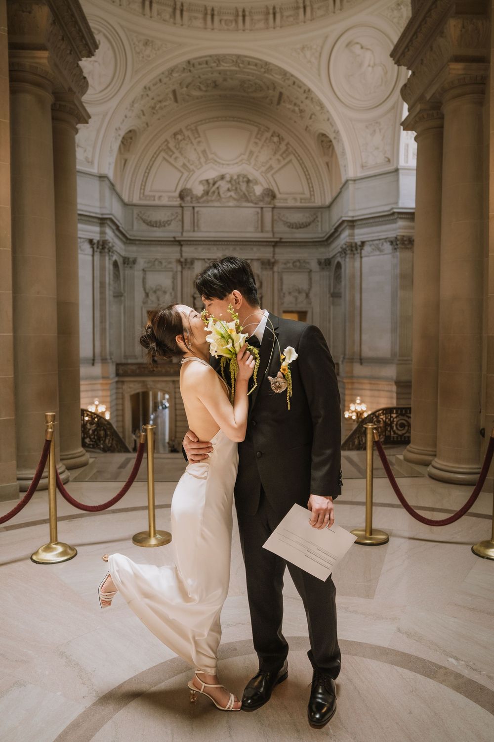A romantic wedding moment inside a grand marble civil building with ornate architecture and golden stanchions.