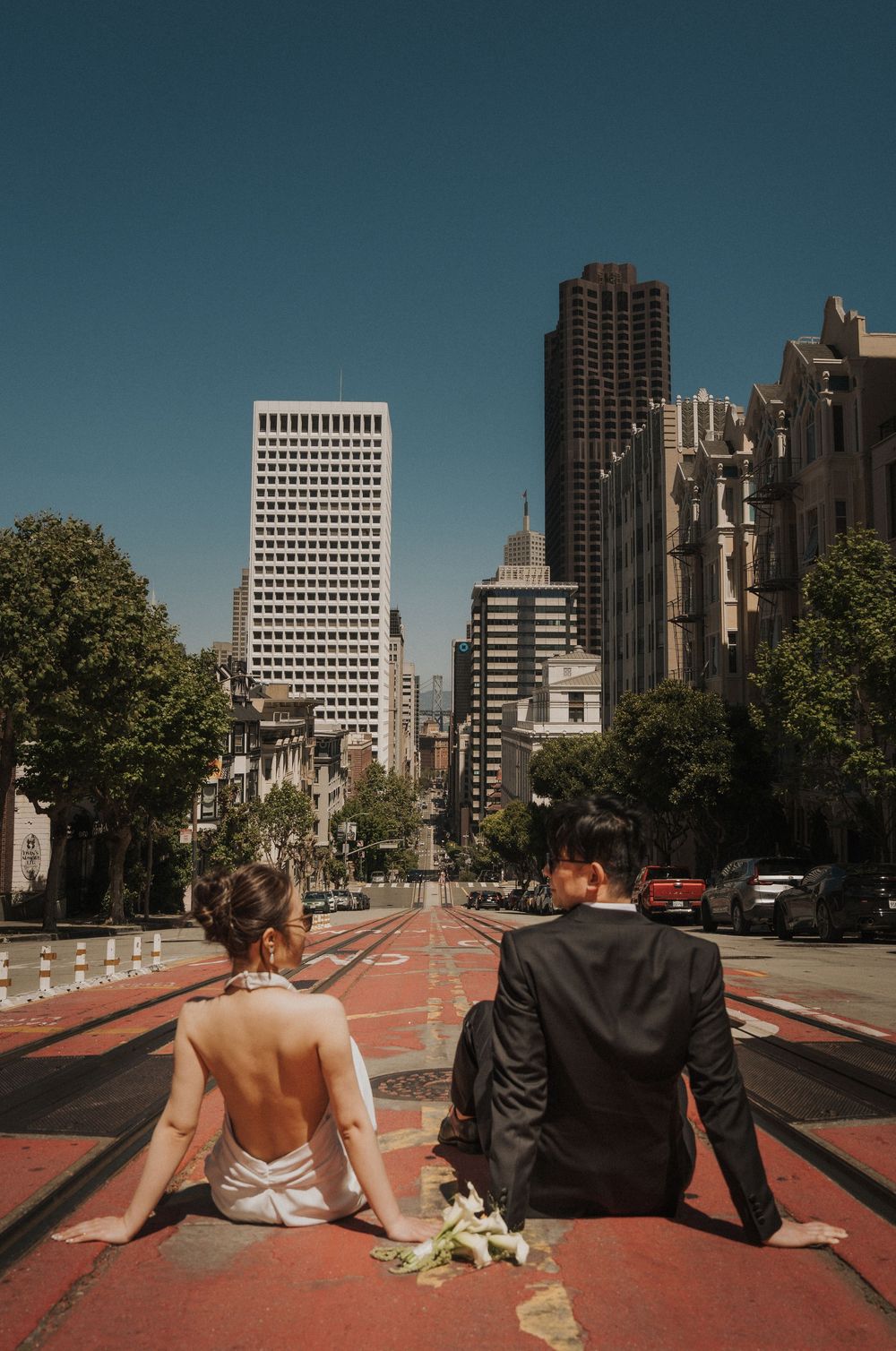 A couple sits back-to-back on a red pathway overlooking a cityscape with modern buildings and blue skies in Montreal.