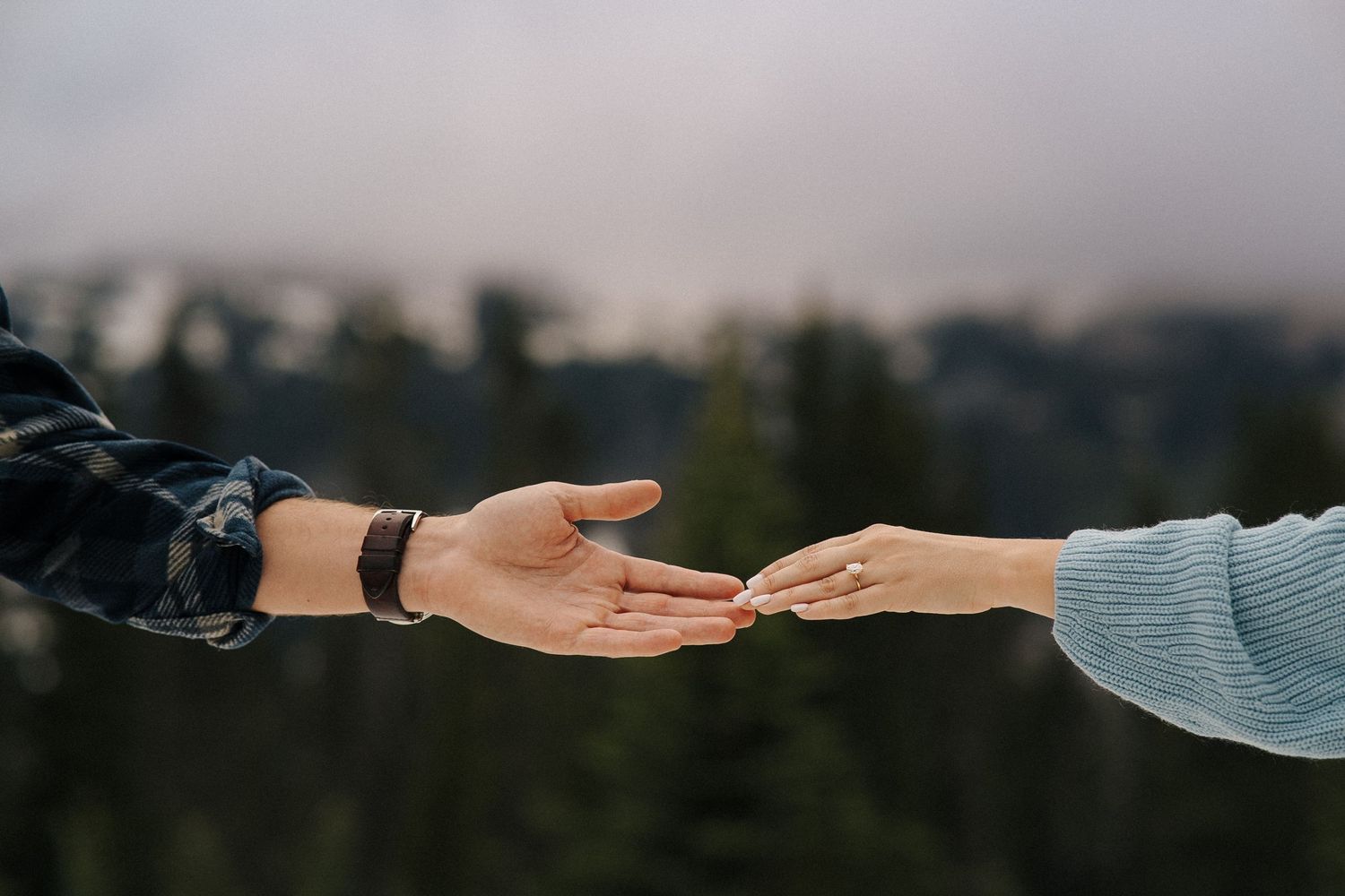Two hands reach out from opposite sides of the frame, symbolizing connection and unity in an outdoor mountain setting.