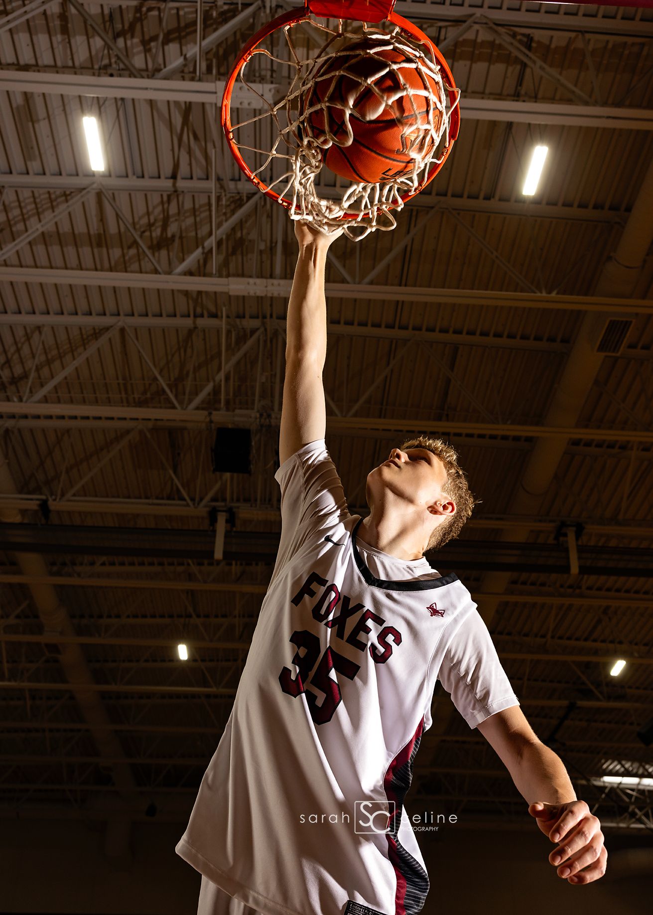 Basketball player completes slam dunk sequence in white jersey against dark indoor arena background.