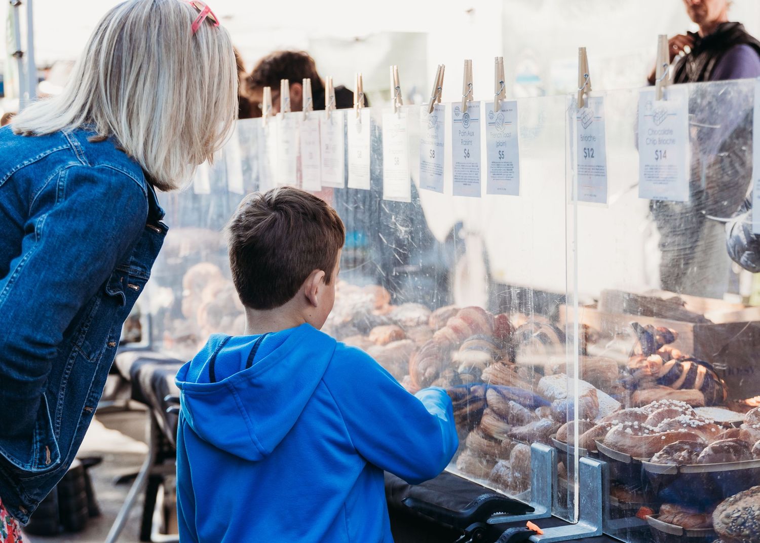 A person in a blue jacket looks at pastries displayed behind glass at a bakery counter.