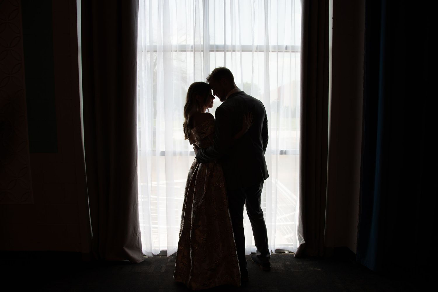 Silhouettes of a couple embracing near a window with soft natural light.