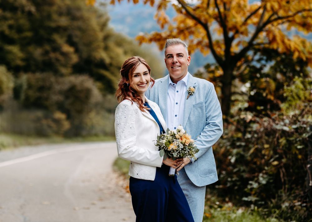 A couple shares a romantic autumn moment surrounded by vibrant fall foliage on a nature path.