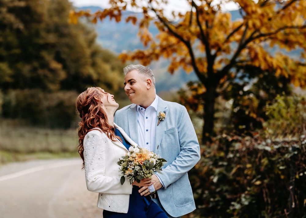A romantic wedding portrait of a couple embracing on a country road surrounded by fall colors.