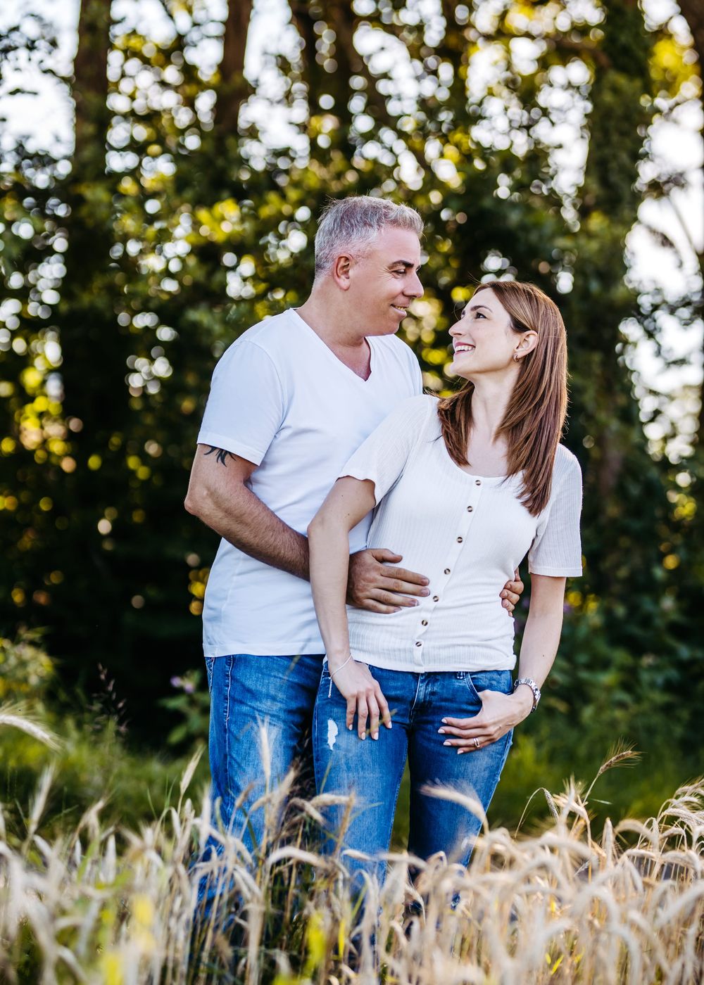 Romantic couple in white shirts embrace in a golden wheat field at sunset.