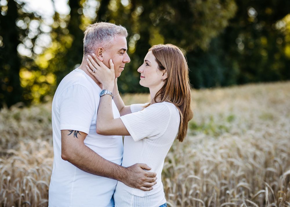 A romantic couple in white outfits embraces in a golden wheat field during sunset.