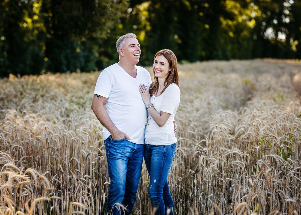 Couple in white shirts and jeans standing together in a golden wheat field at sunset.