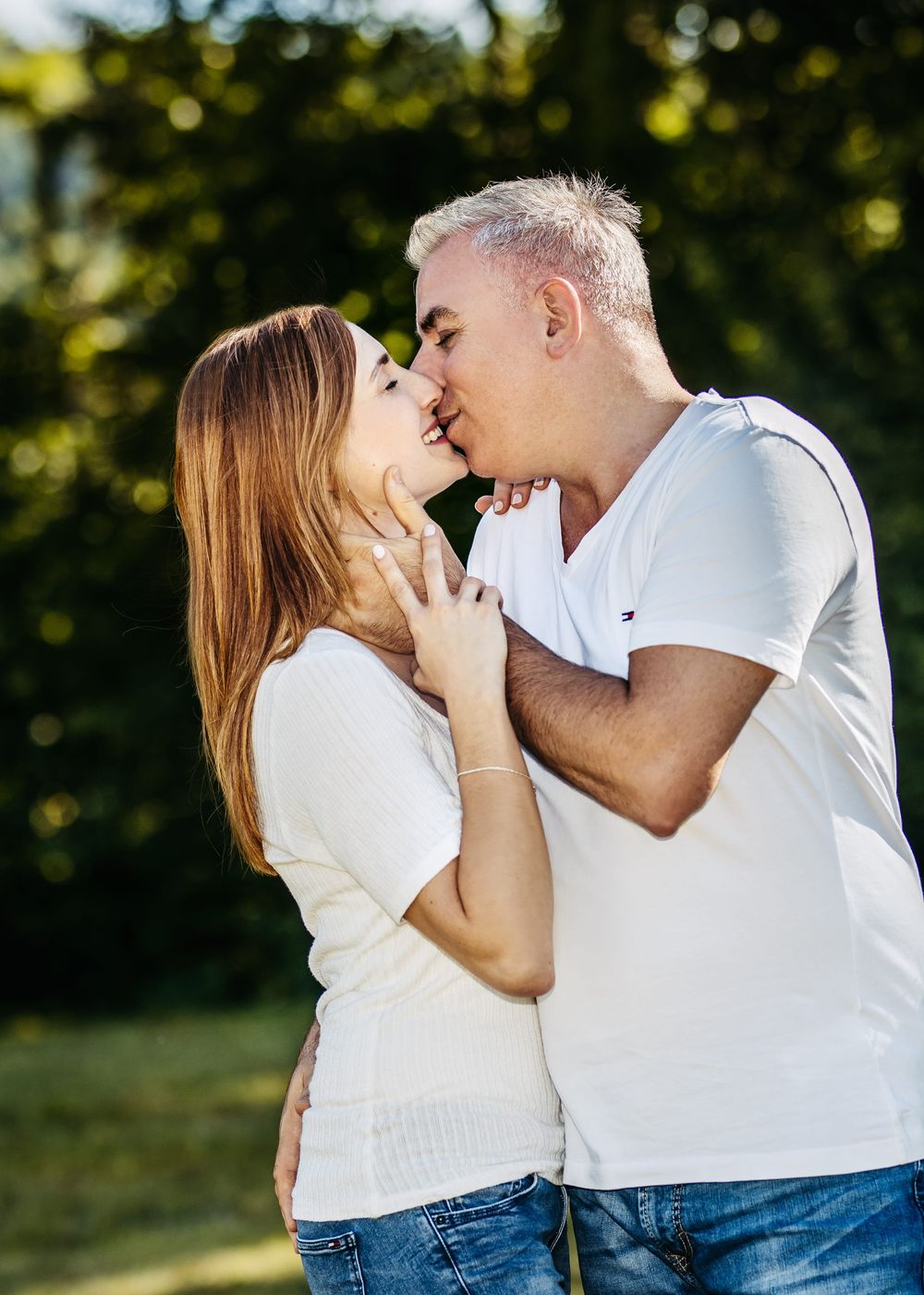 Couple sharing intimate moments in white shirts against a natural outdoor backdrop.