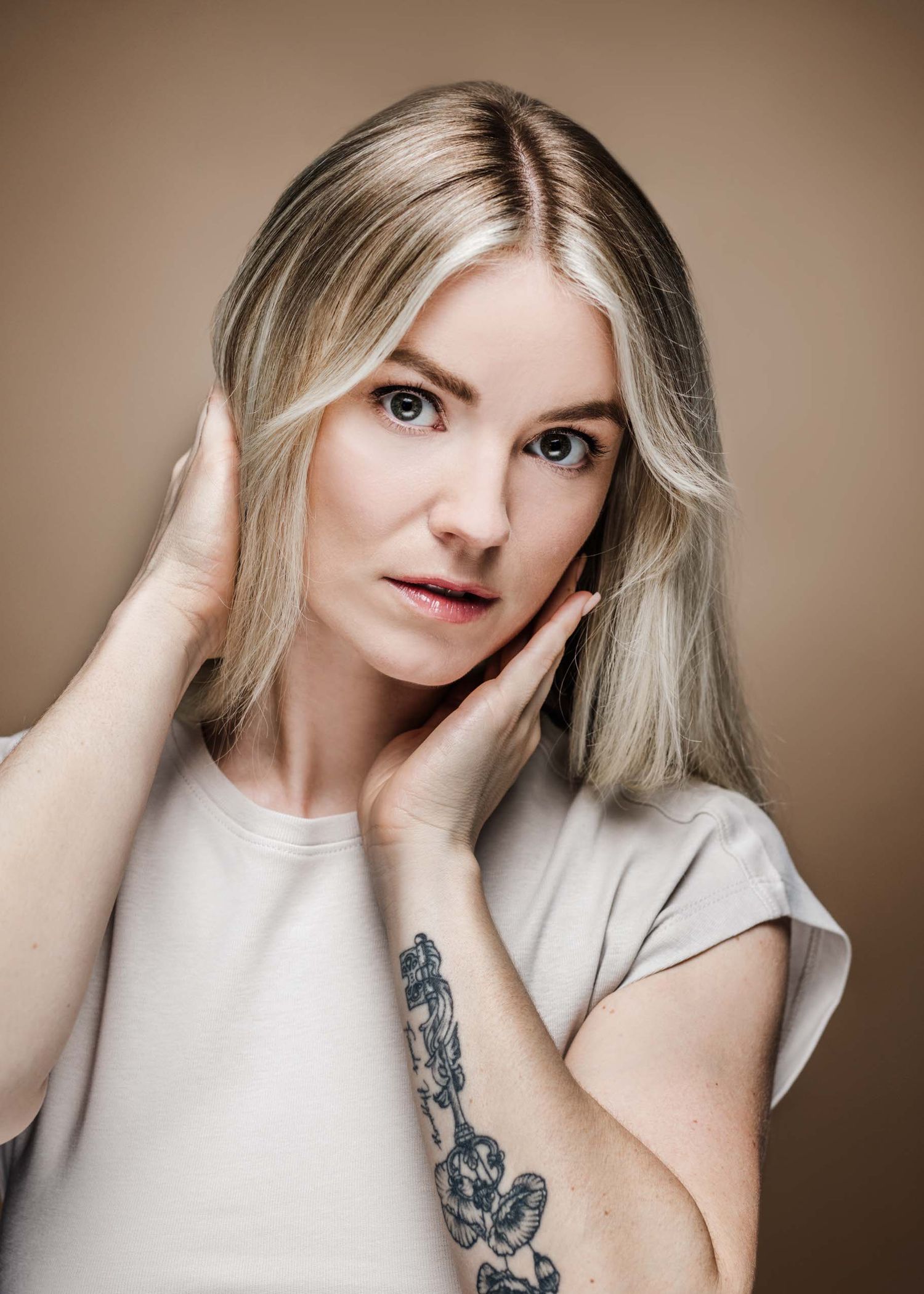 Artistic portrait series showing expressive poses against neutral background wearing white top with dark tattoo detail.