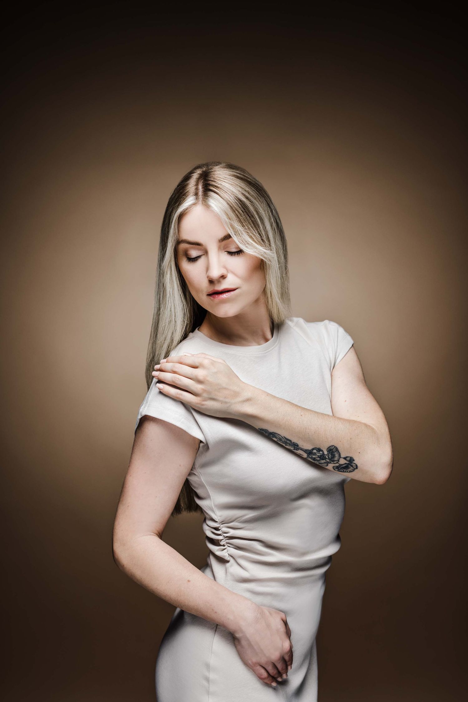 A person in a white sleeveless top poses expressively against a dark brown background in an artistic photo series.