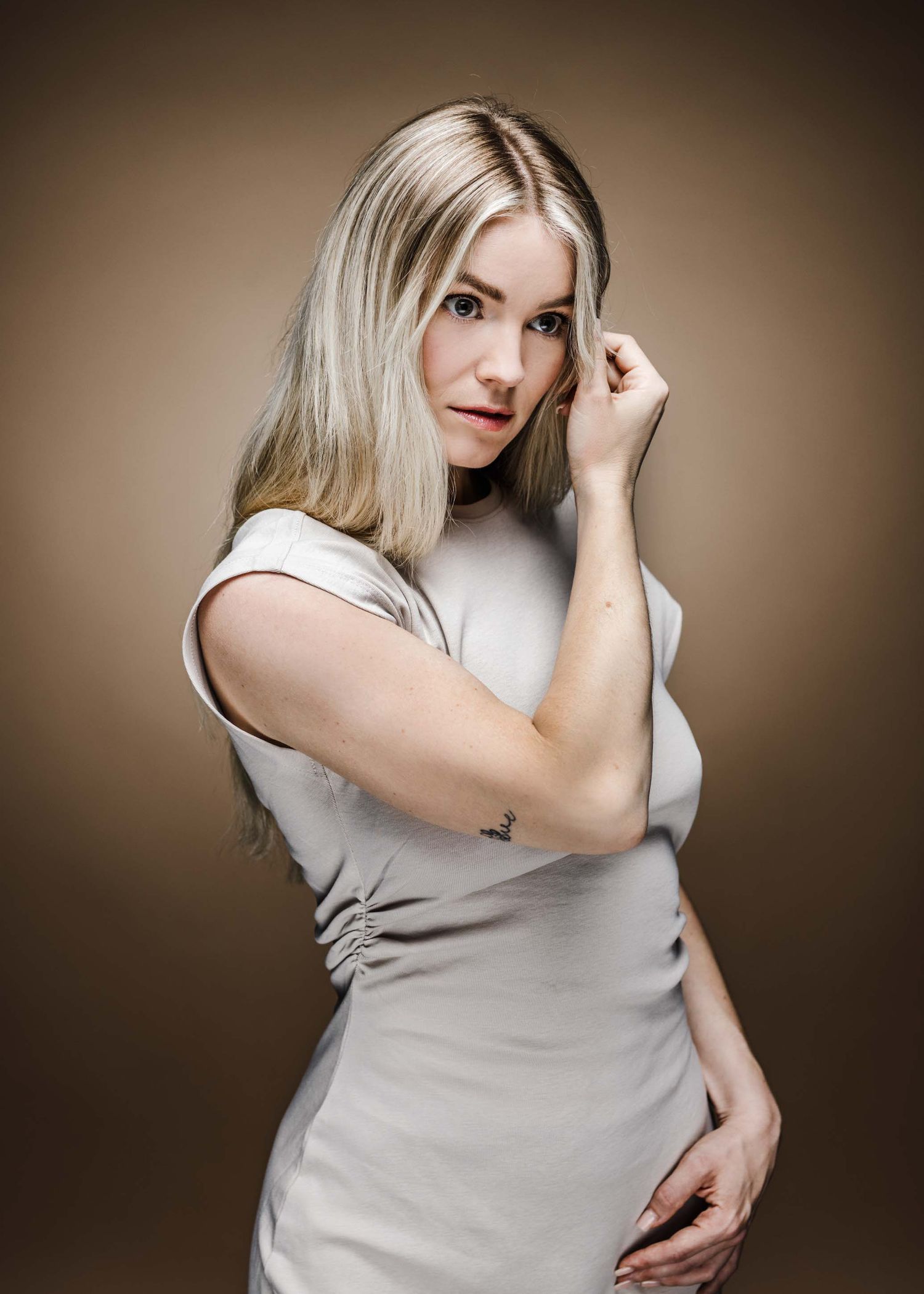 A person in a light gray t-shirt poses against a brown background in an artistic portrait series.