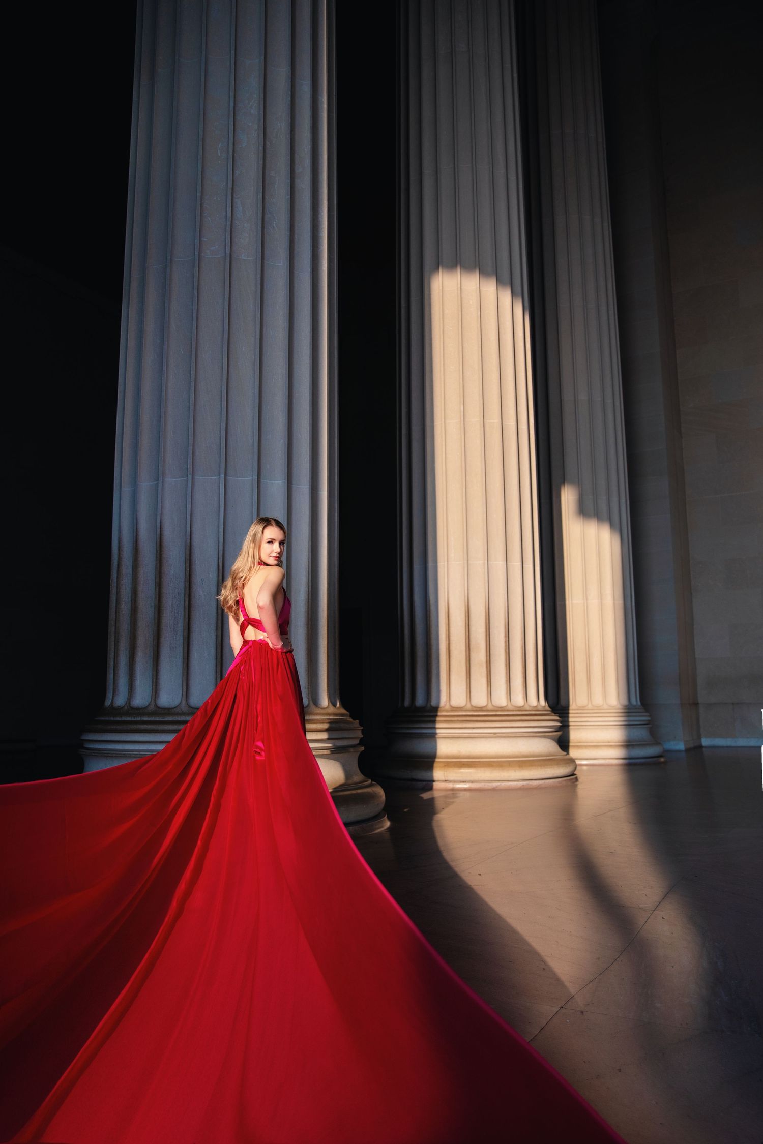 A flowing red gown creates dramatic contrast against classical stone columns in dramatic lighting. Flying Dress Photo