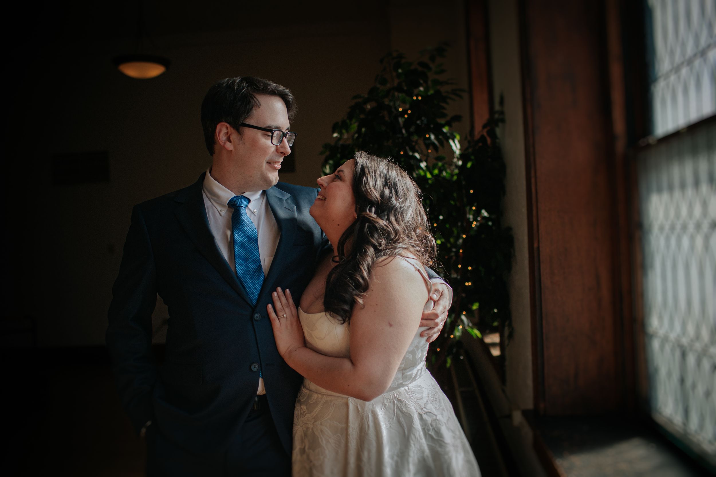 A romantic moment between newlyweds in a dimly lit rustic venue with vintage windows and greenery decor.