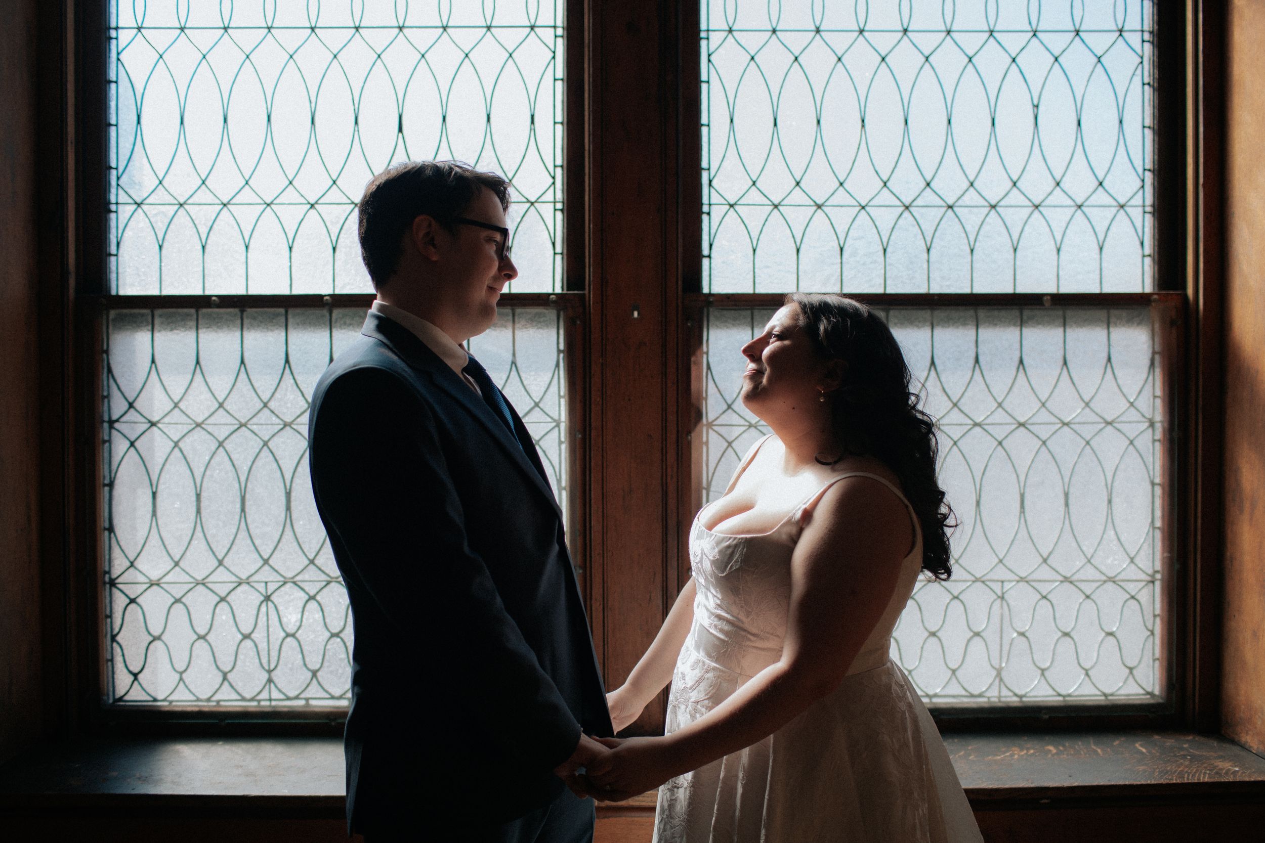 Silhouetted couple stands in front of a geometric patterned window at sunset creating a romantic atmosphere.