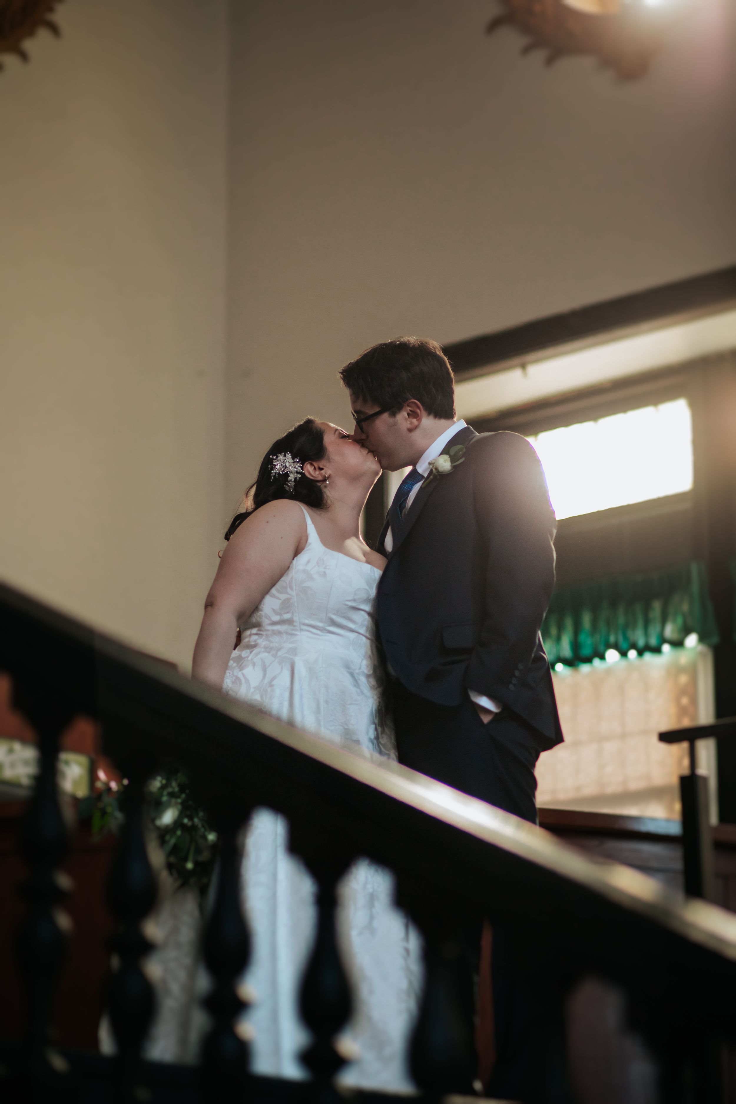 A romantic wedding moment captured on a staircase with soft lighting and elegant decor in the background.