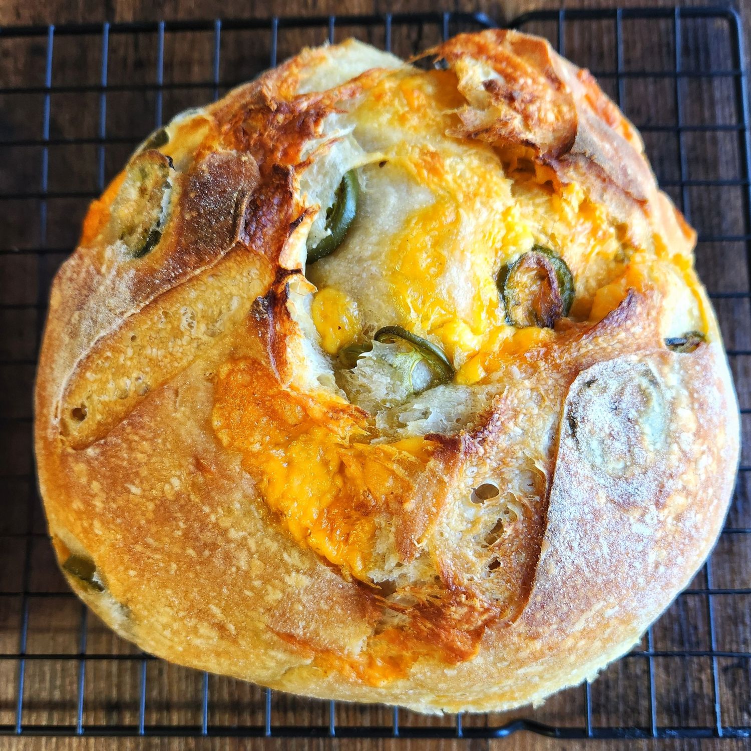 Fresh baked jalapeno cheddar sourdough bread cooling on a wire rack with melted cheese and golden crust.