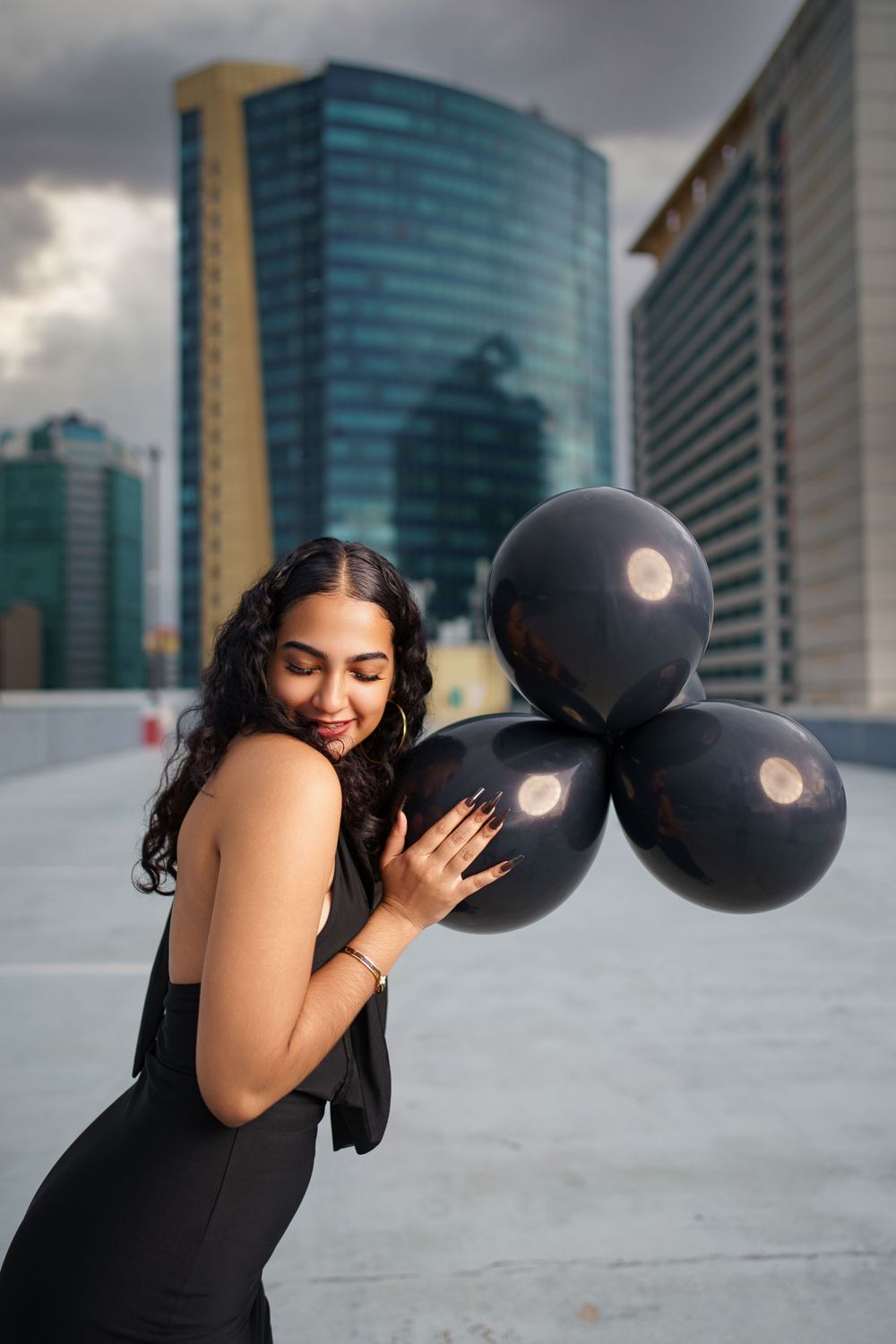Artistic portrait session with black balloons on rooftop featuring dramatic cloudy sky backdrop.