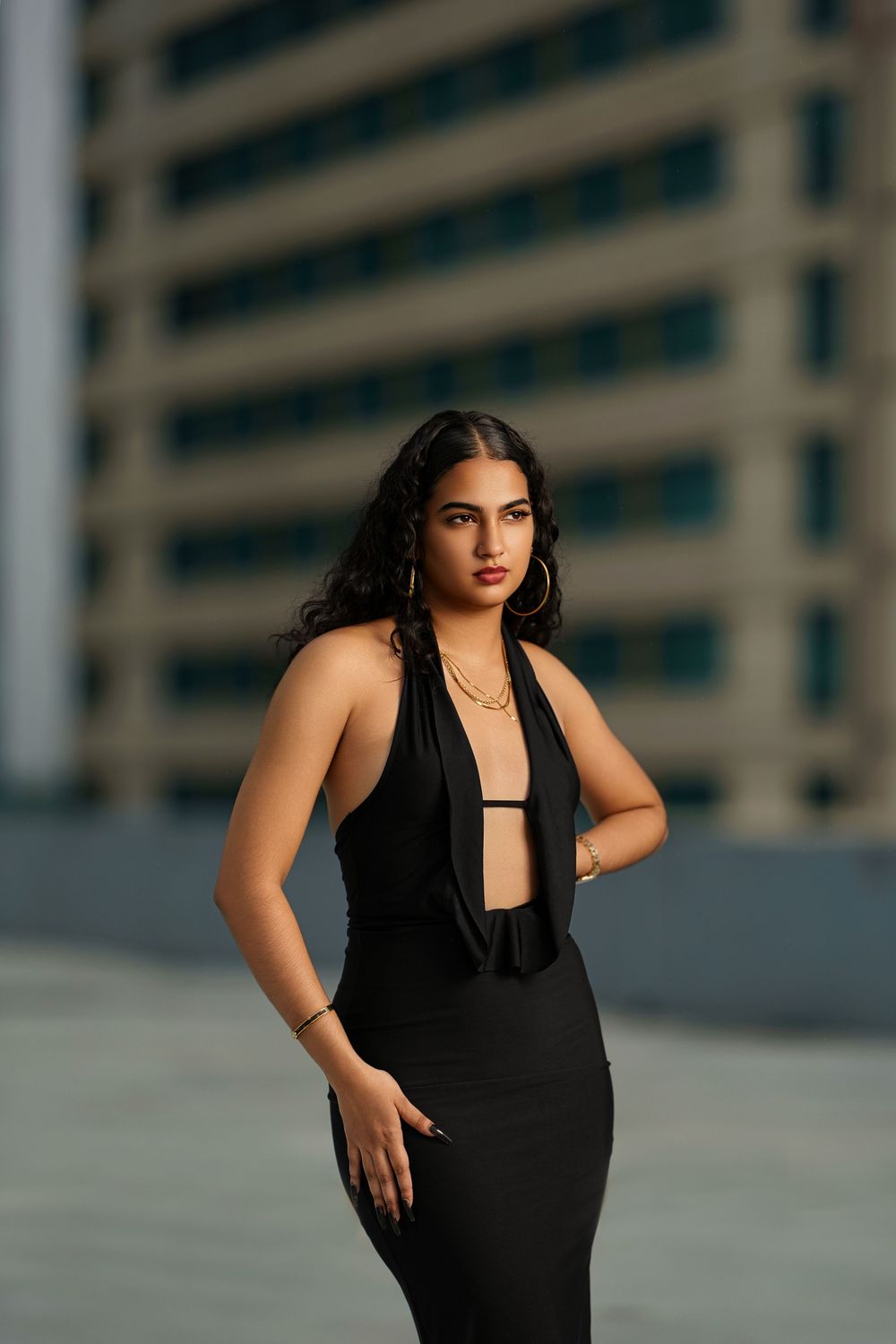 Elegant fashion portrait featuring a black plunging neckline dress against an urban backdrop with modern architecture.