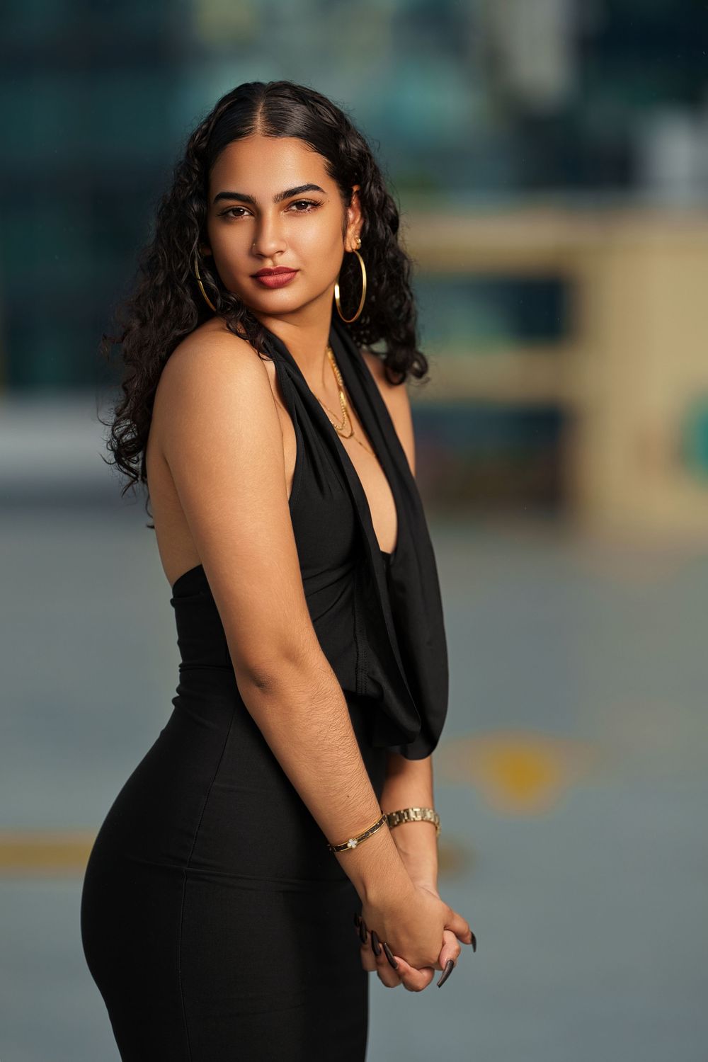 Woman in elegant black dress poses on urban rooftop during golden hour.
