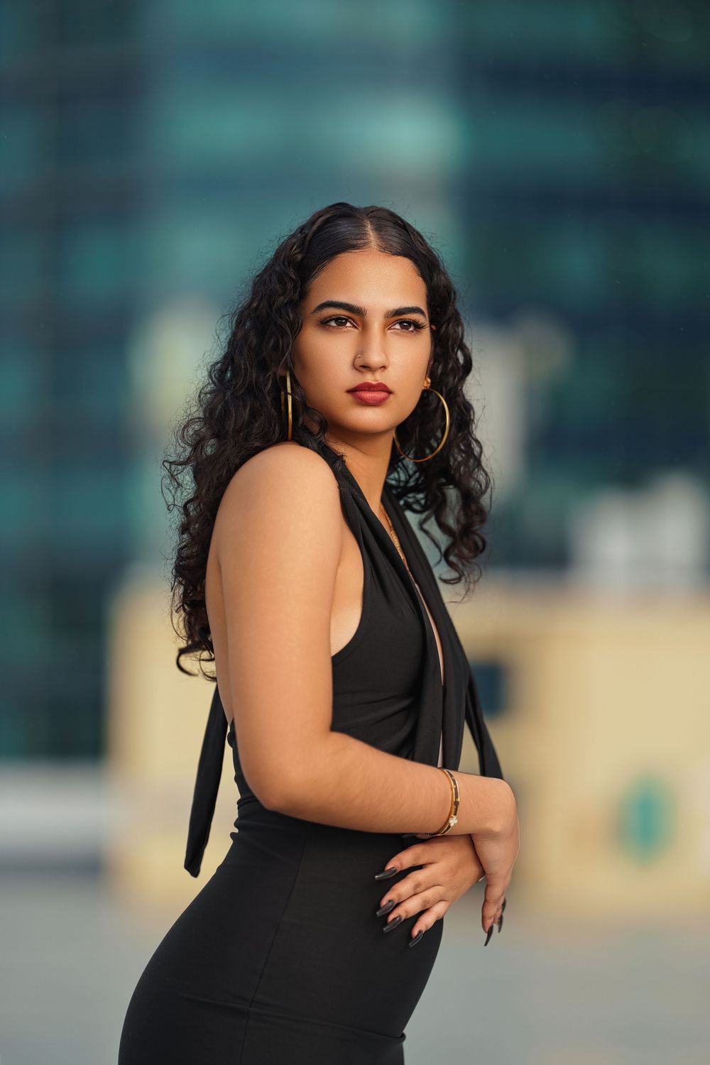 Stylish portrait showcasing a fitted black dress with statement jewelry against blurred city buildings.