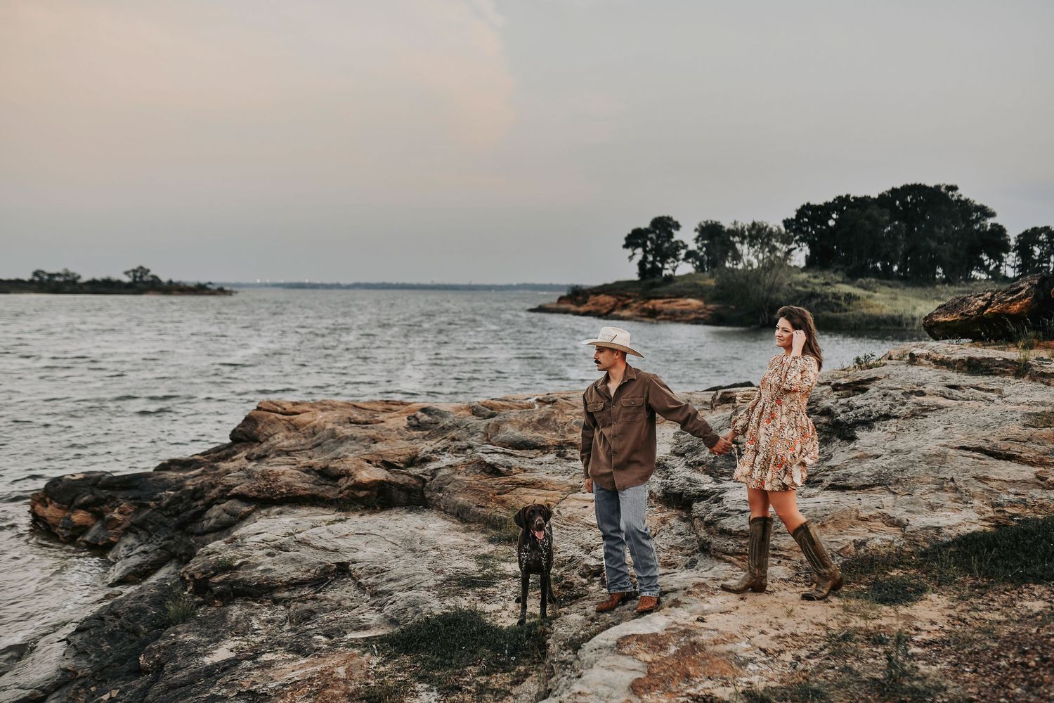 Couple walking their dog overlooking a rocky lakeside during an engagement session in Flower Mound, Texas