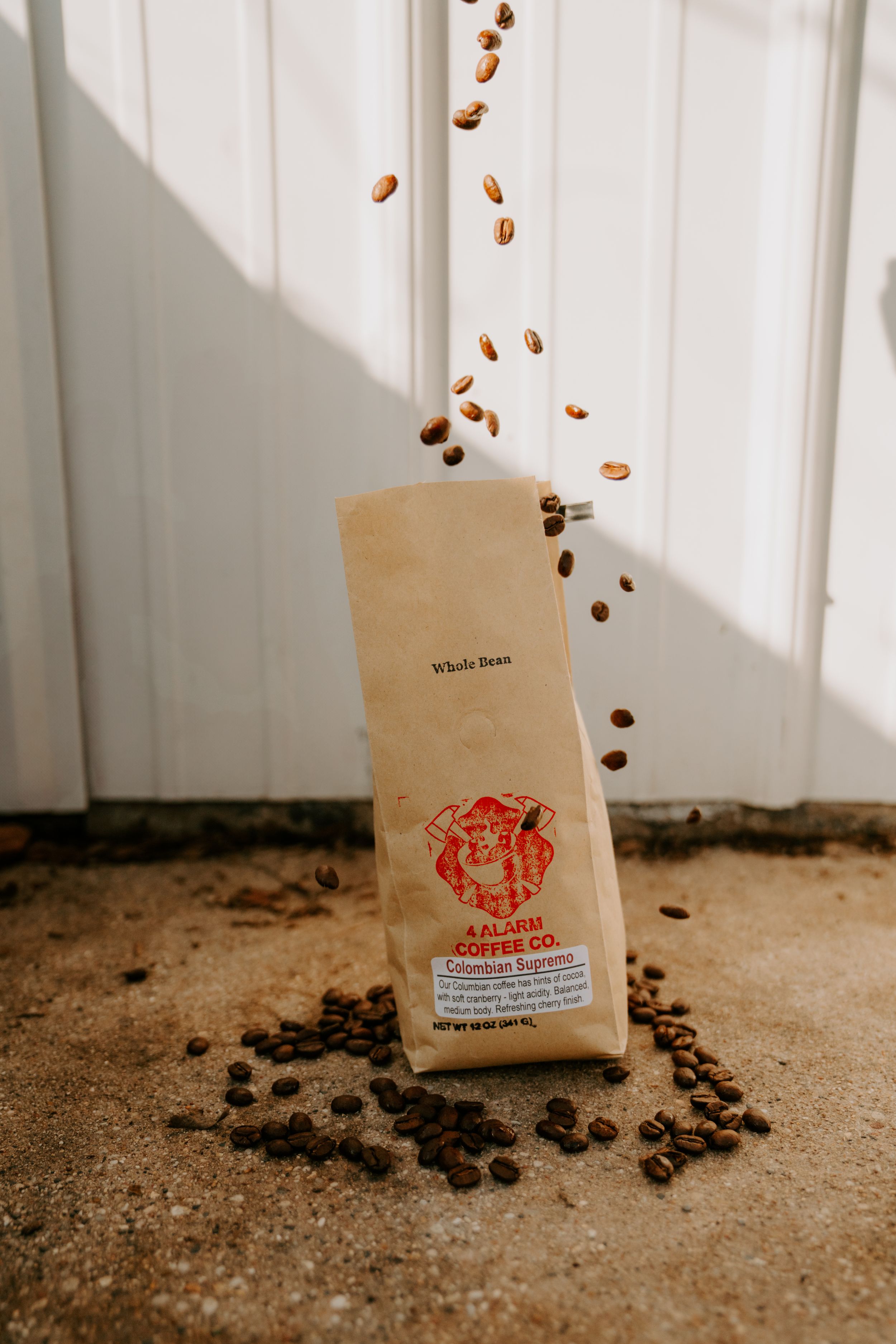 Coffee beans falling from a brown paper bag with red logo branding.