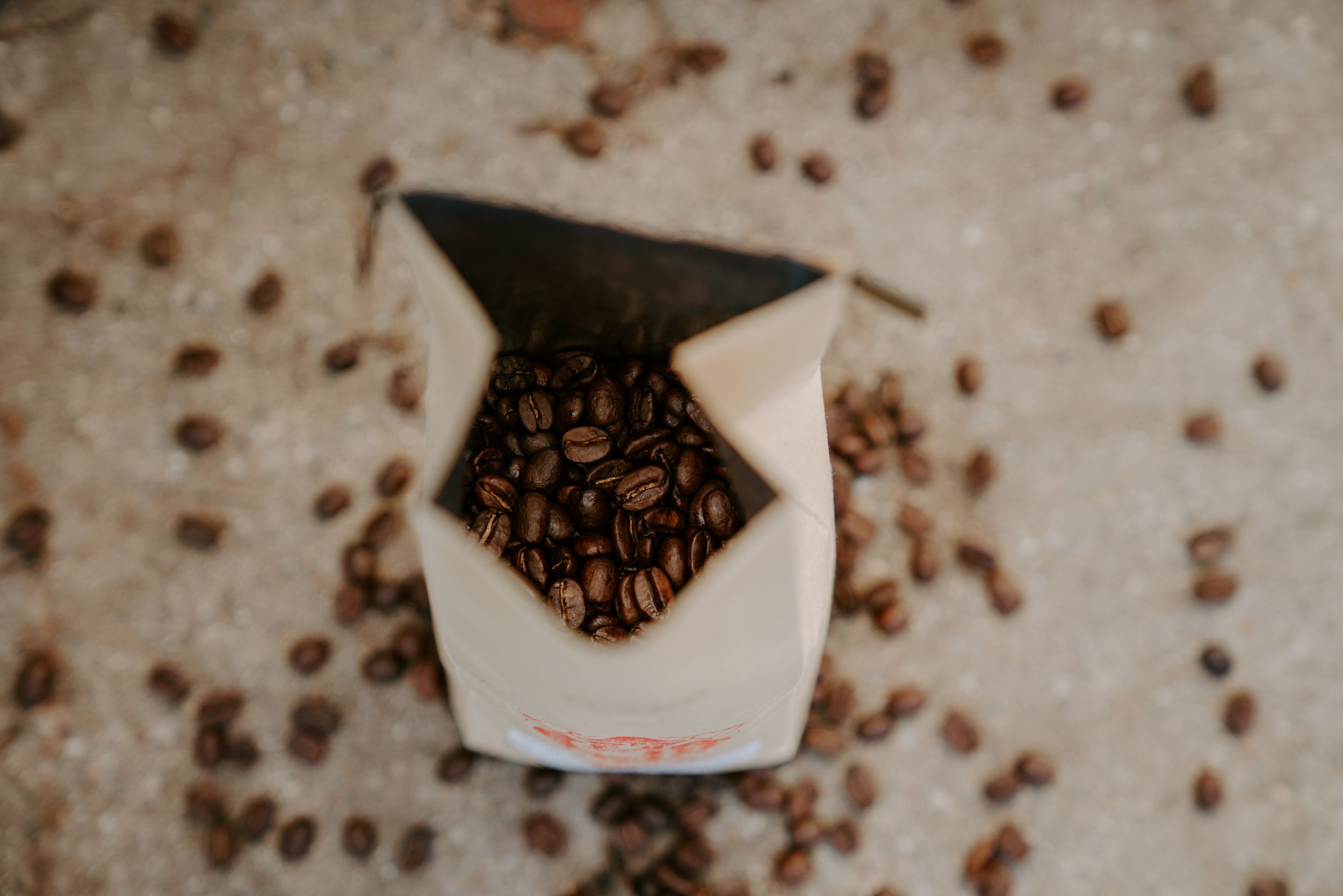 Scattered coffee beans on concrete surface with branded packaging.