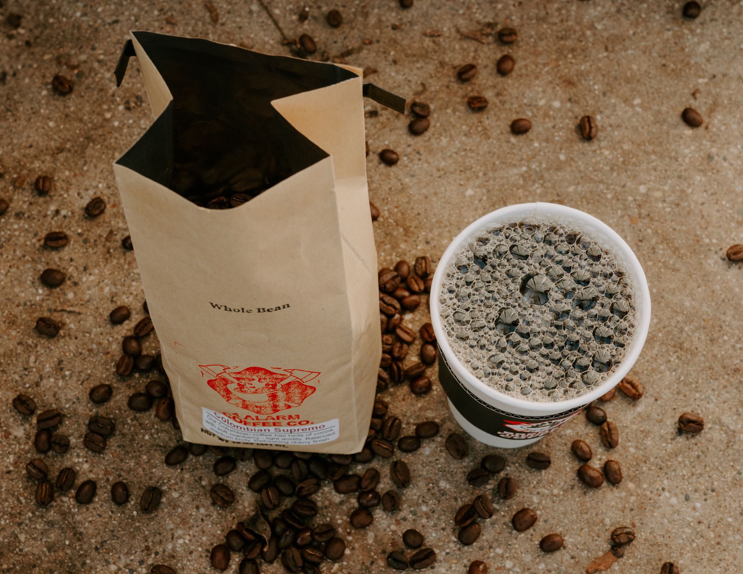 Coffee beans scattered around branded cups and packaging on rustic background.