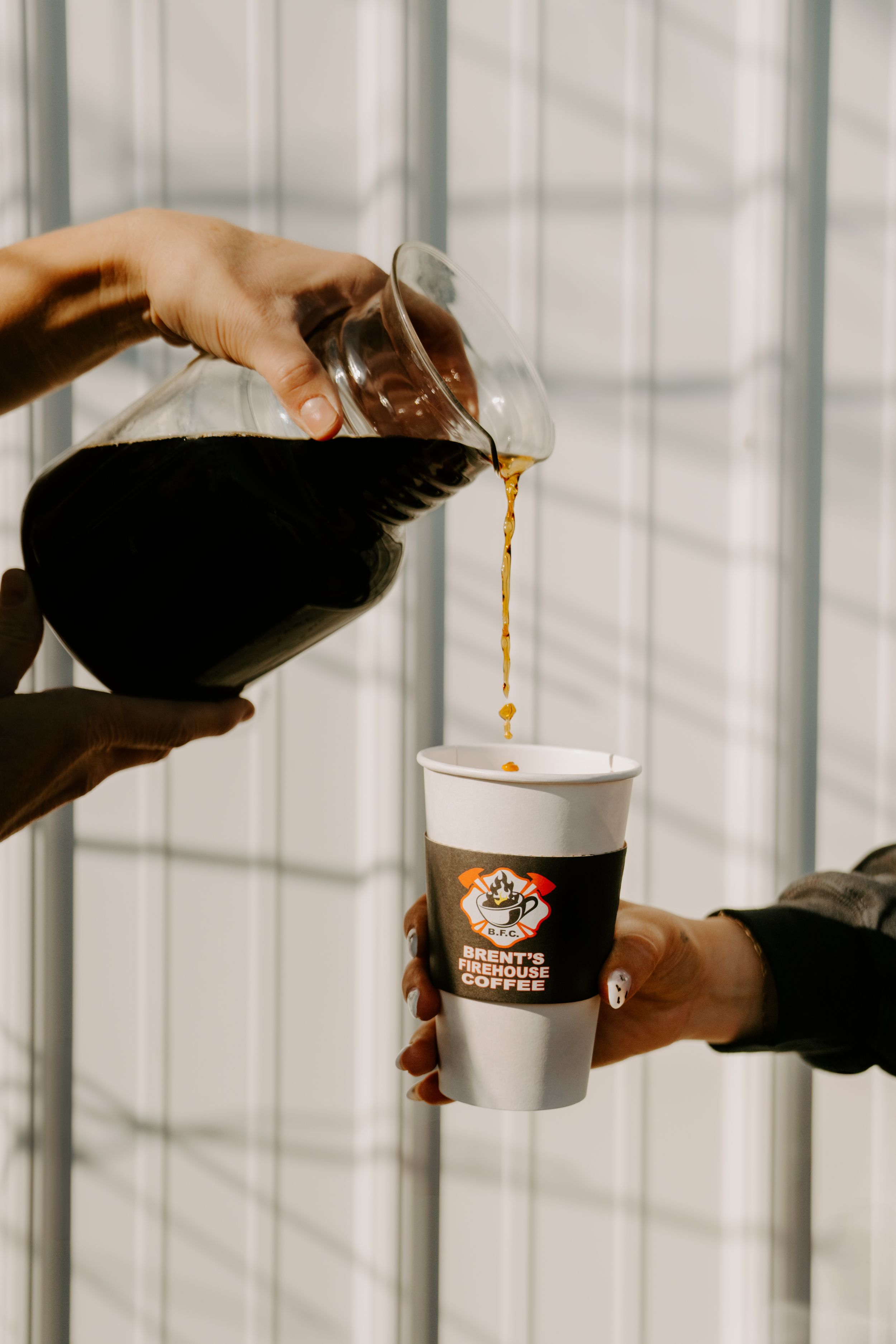 Hands pouring coffee into branded cups against white window background.