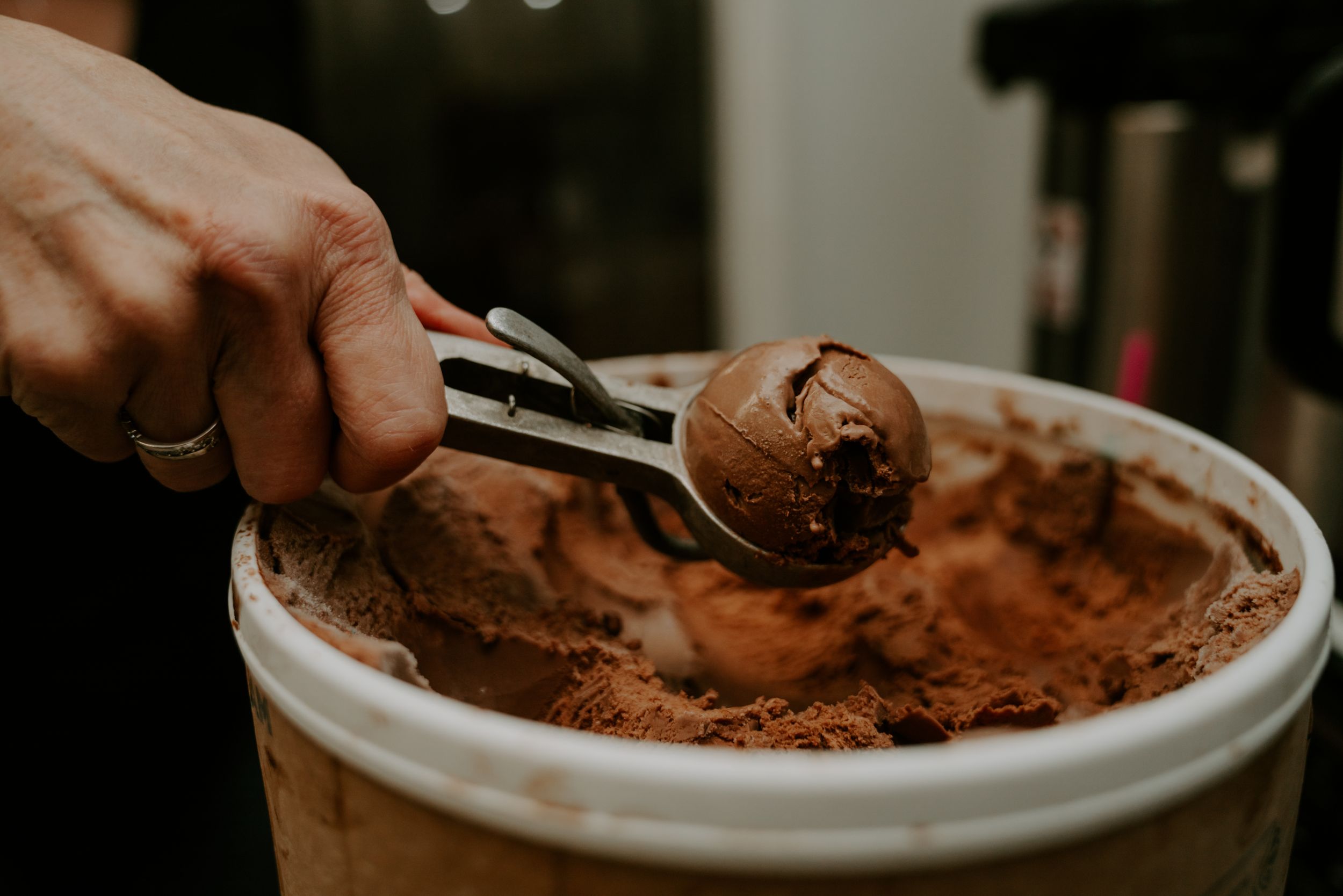 Dark chocolate powder being scooped into a white ceramic container.