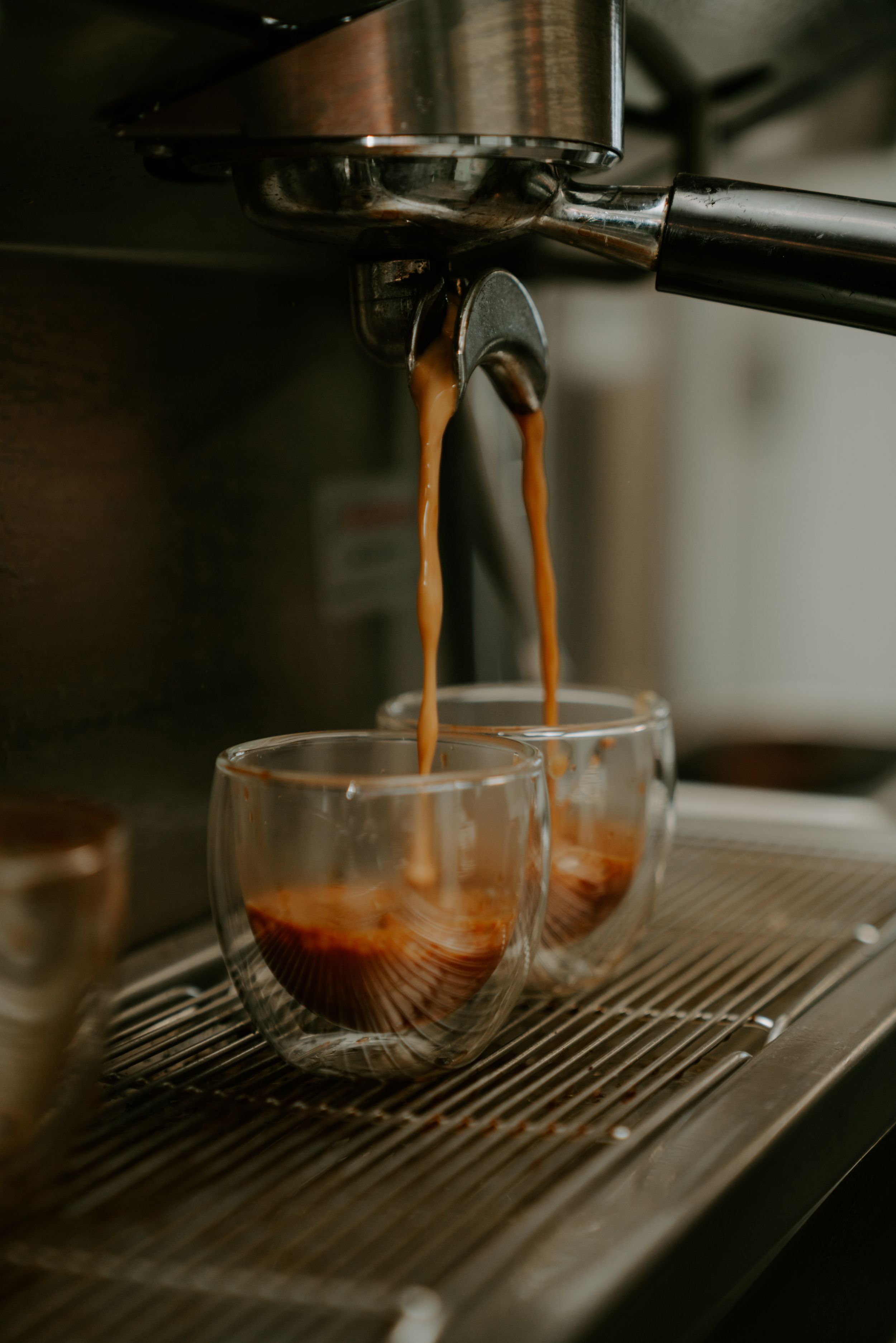 Rich espresso coffee pouring from a machine into a clear glass cup.