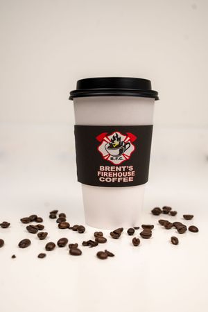 Black coffee cups with Brent's Firehouse Coffee branding scattered among coffee beans.