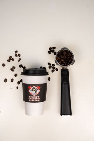 Coffee beans scattered around a coffee cup and grinder on white background.