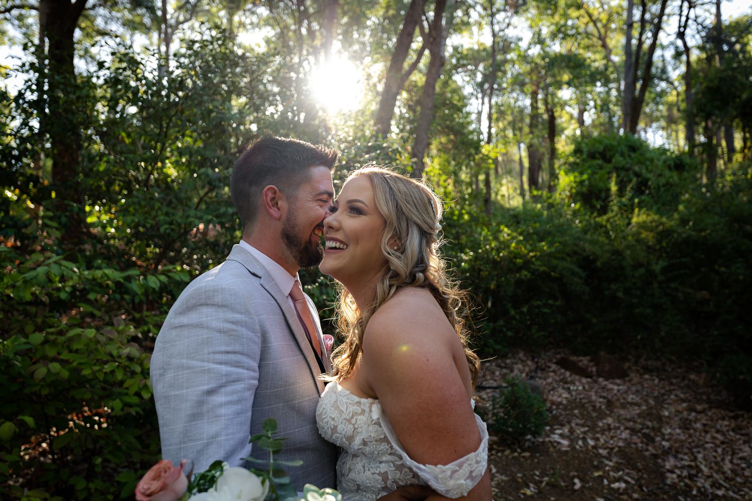 A couple shares romantic moments in a sunlit forest setting during their wedding photoshoot.