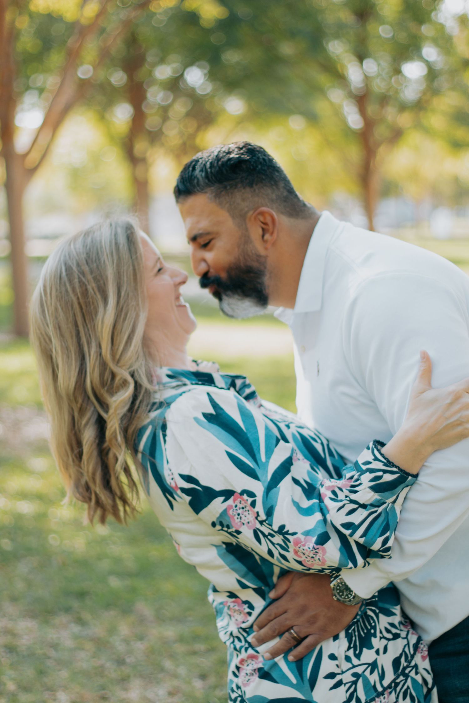 Couple in romantic embrace outdoors with woman wearing floral blue and white dress against natural background.